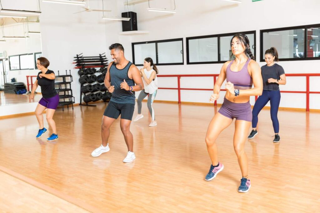 Two adult dancers practice basic salsa steps and a turn on a clear indoor dance floor.