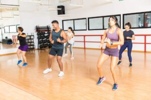 Two adult dancers practice basic salsa steps and a turn on a clear indoor dance floor.